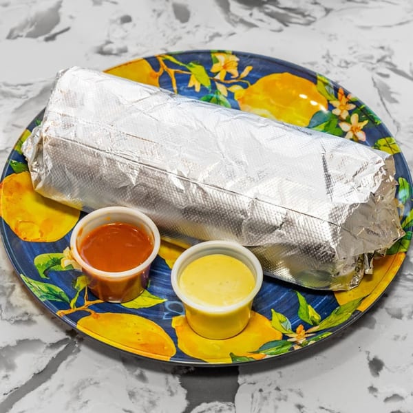 A foil-wrapped burrito from Tacos Don Chai on a lemon-patterned plate with two sauce cups.