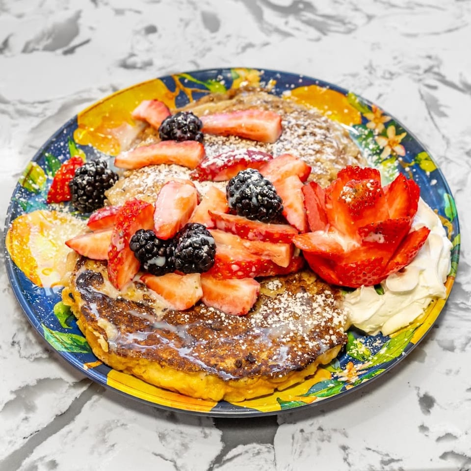 Pancakes topped with strawberries, blackberries, powdered sugar, and whipped cream on a colorful plate.