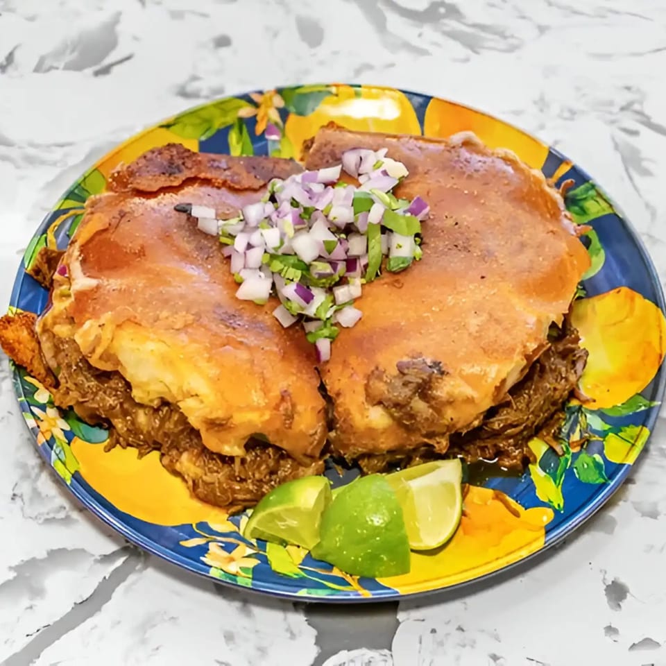 Two Mexican burritos topped with diced red onions and cilantro, served with lime wedges.
