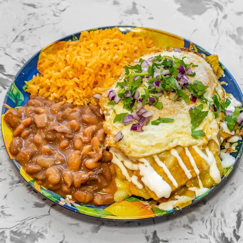 Mexican breakfast plate with chilaquiles topped with fried eggs, rice, and refried beans.